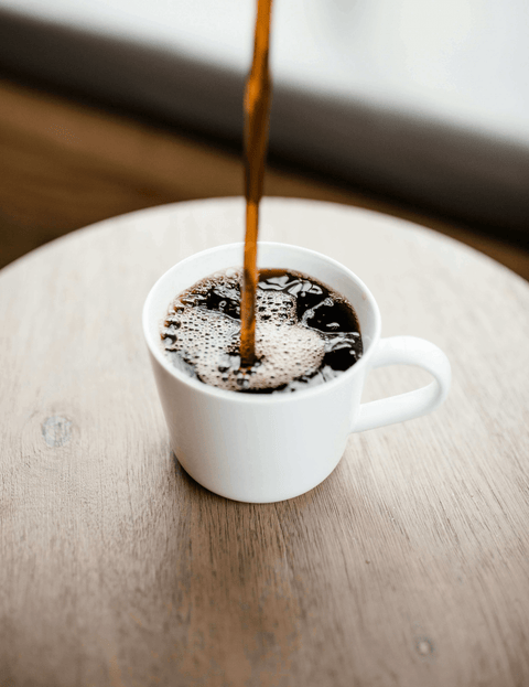 Image of coffee being poured into a coffee cup on a wooden table.